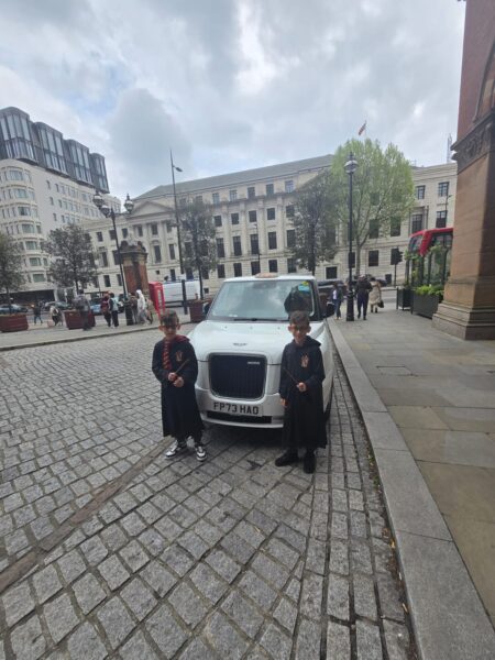 Visitors enjoying day tours from London UK with London Sightseeing Taxi Tours, posing in Harry Potter wizard robes beside a wheelchair-accessible taxi in iconic London square