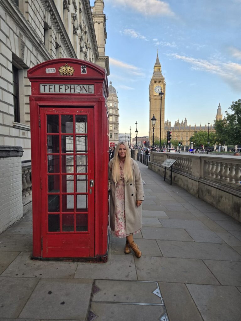 Tourist posing in front of iconic red phone booth with Big Ben during british museum guided tour in London, offered by accessible London Sightseeing Taxi Tours for up to six people