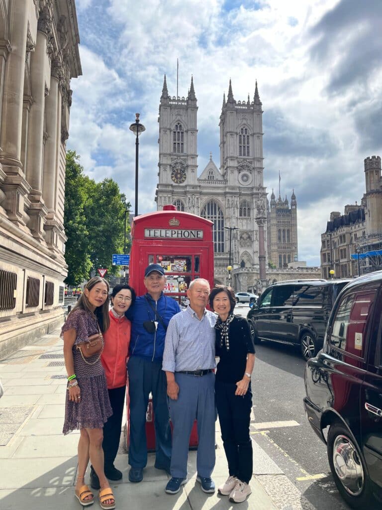 Group of tourists enjoying guided tours of England with London Sightseeing Taxi Tours, posing by iconic red phone booth in front of Westminster Abbey