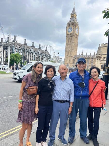 london sightseeing tour packages featuring a group of tourists posing with a wheelchair-accessible taxi tour van in front of Big Ben and the London Eye, ideal for family group tours in London