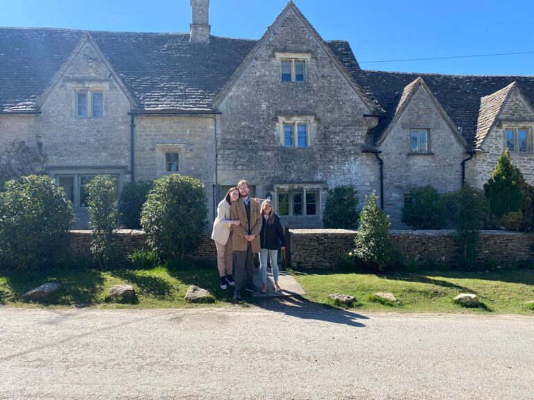Group of tourists enjoying walking tours in England, standing in front of a picturesque stone cottage in the Cotswolds