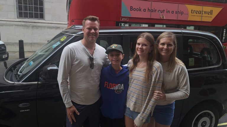 Local guides leading a family on a London sightseeing taxi tour in a black cab near iconic red double-decker bus