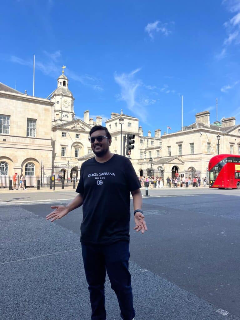 Visitors on a london sightseeing bus tour posing in front of Buckingham Palace with iconic red double-decker bus and historic London architecture